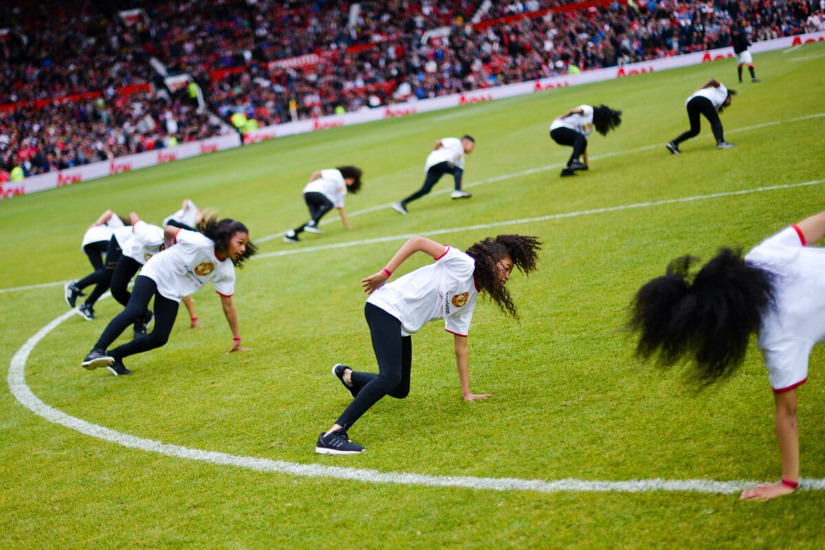 A photo of a group of children dancing in the centre circle of Old Trafford football stadium, Manchester at our Red Heart United event in 2015